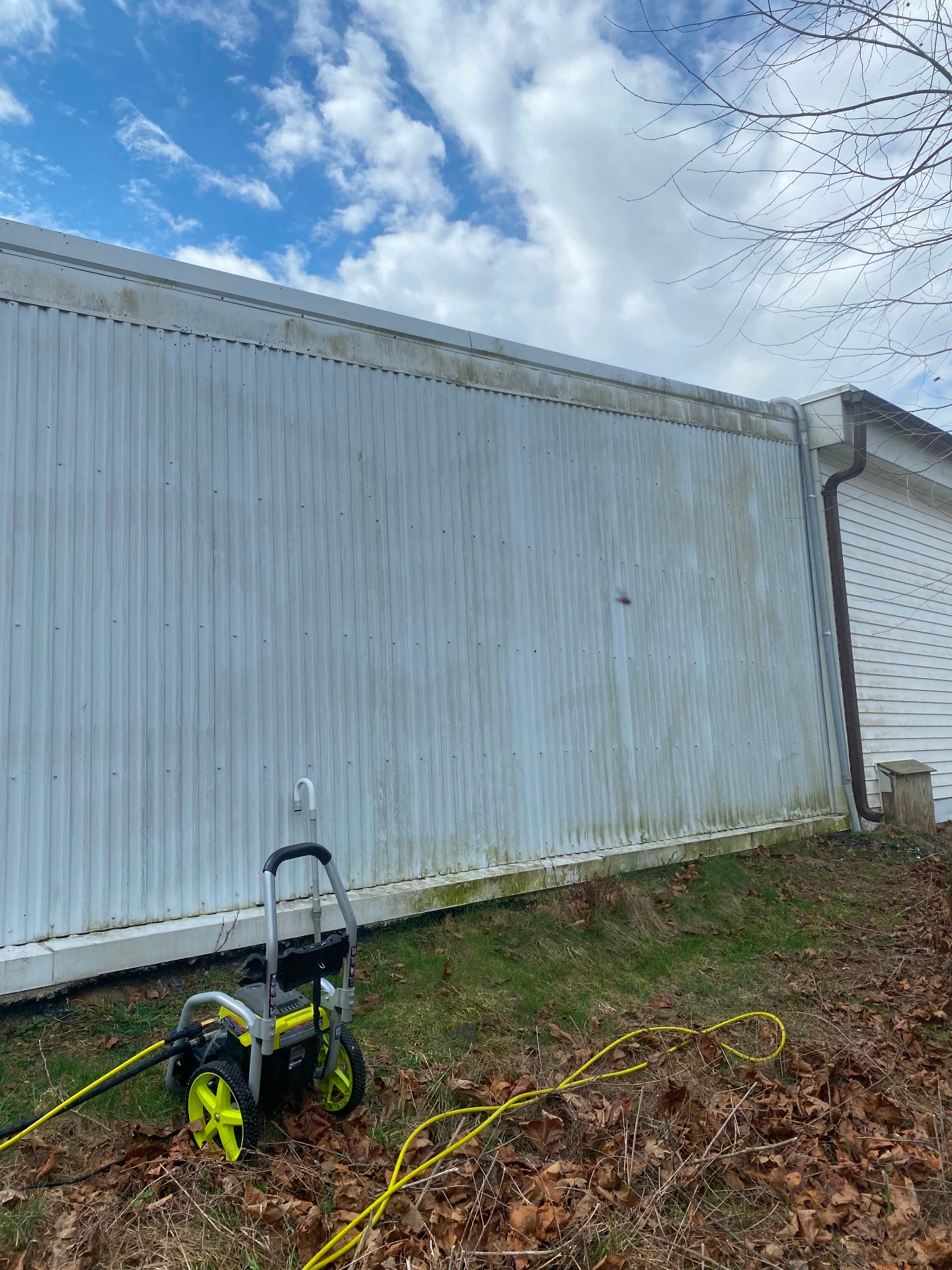 Metal-sided outbuilding with heavy green algae and grime along the top edge before soft washing